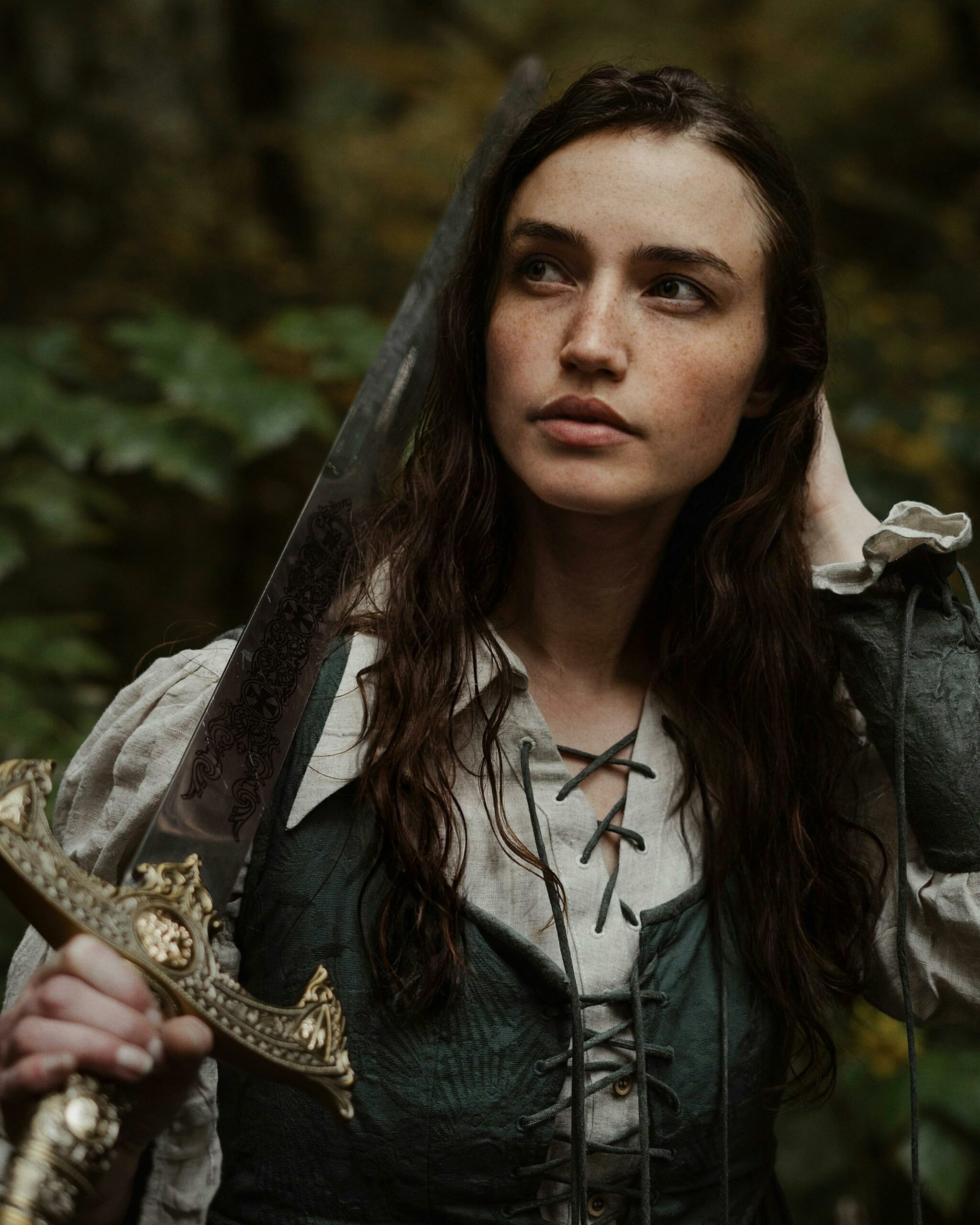 A captivating portrait of a woman in medieval attire holding a sword in a forest setting.